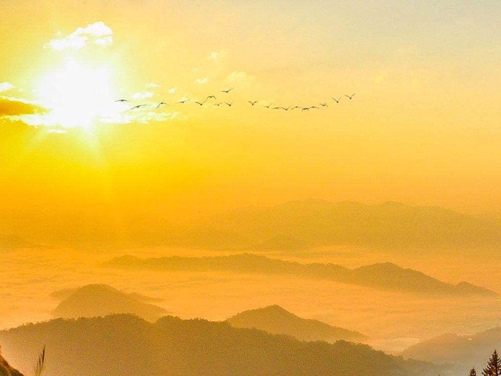 Le soleil se lève sur des montagnes de brume, un vol d’oiseaux traverse le ciel